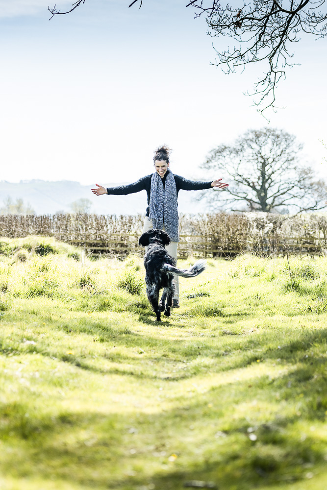 woman in country with open arms welcoming her dog